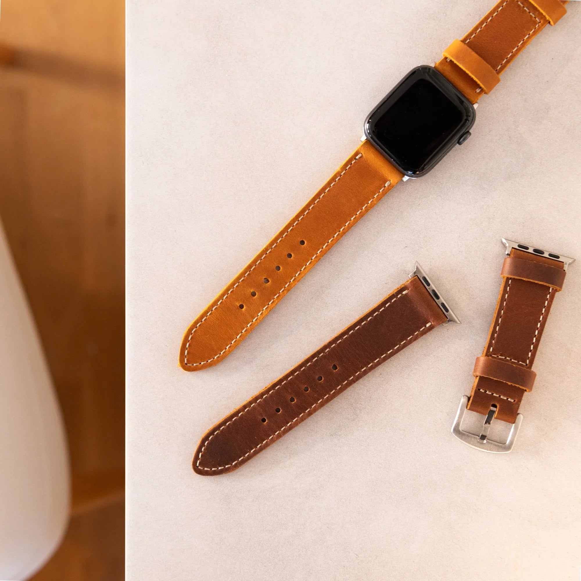 Full-grain leather Apple Watch straps in tan and brown on a light surface from Yukon Bags.